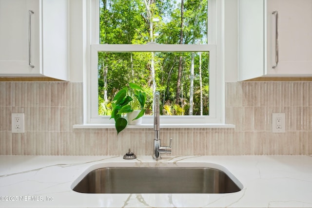 kitchen view of a sink, white cabinets, tasteful backsplash, and light stone countertops