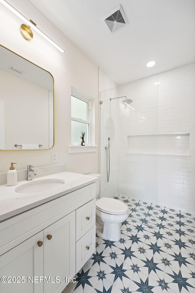 full bath with toilet, a tile shower, vanity, and tile patterned floors