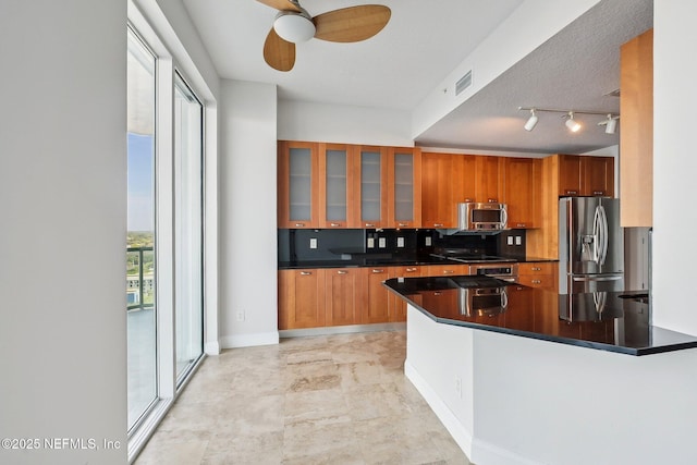 1431 Riverplace Blvd Unit 1707, Jacksonville, FL 32207 - kitchen featuring stainless steel appliances, brown cabinets, dark countertops, ceiling fan, and glass insert cabinets
