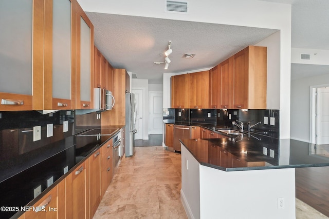 1431 Riverplace Blvd Unit 1707, Jacksonville, FL 32207 - kitchen with appliances with stainless steel finishes, brown cabinets, a peninsula, dark countertops, and decorative backsplash
