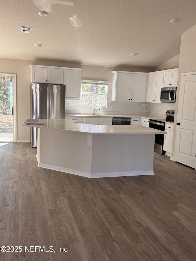 47 Laguna Forest Trl, Palm Coast, FL 32164 - kitchen with appliances with stainless steel finishes, a kitchen island, dark wood-type flooring, backsplash, and a textured ceiling