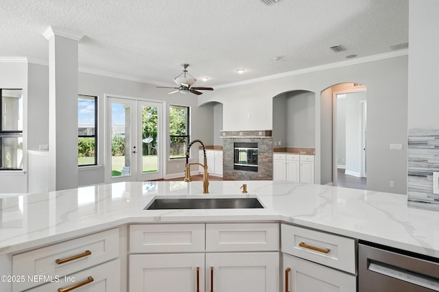 10065 Ecton Ln, Jacksonville, FL 32246 - kitchen with a sink, stainless steel dishwasher, white cabinetry, a textured ceiling, and a glass covered fireplace