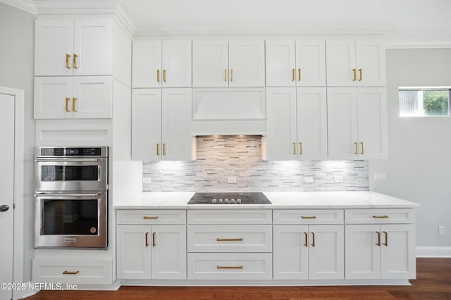 10065 Ecton Ln, Jacksonville, FL 32246 - kitchen with black electric cooktop, double oven, white cabinets, premium range hood, and decorative backsplash