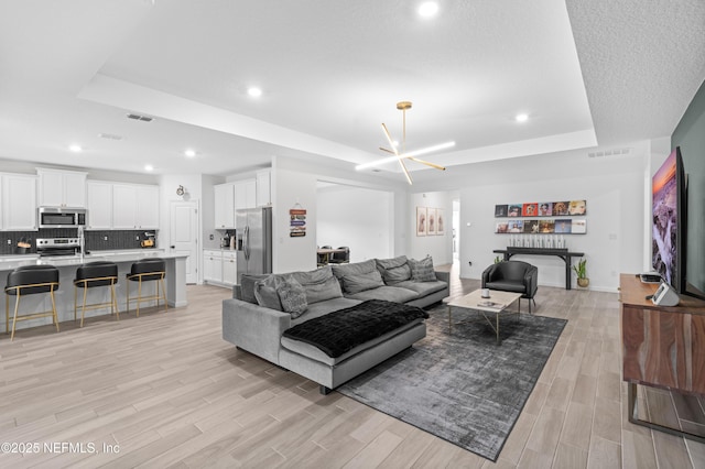 7242 Calamint Ave, Jacksonville, FL 32219 - living room featuring a raised ceiling, light wood-style flooring, recessed lighting, a chandelier, and baseboards