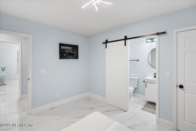 619 S 10th St, Fernandina Beach, FL 32034 - unfurnished bedroom featuring light marble finish flooring, a barn door, baseboards, connected bathroom, and a sink