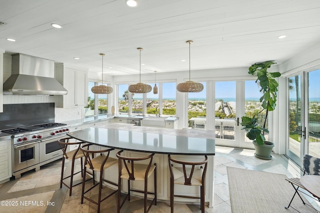 816 Ocean Front, Neptune Beach, FL 32266 - kitchen featuring range with two ovens, wall chimney range hood, backsplash, a kitchen island, and a breakfast bar