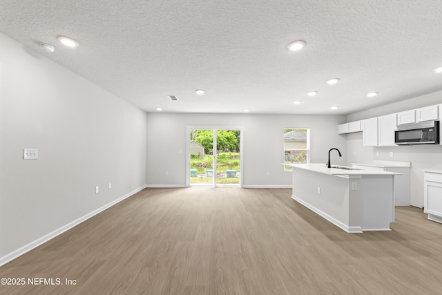 5969 Flicker Ave, Jacksonville, FL 32219 - kitchen featuring stainless steel microwave, a sink, light wood-style flooring, a textured ceiling, and a center island with sink