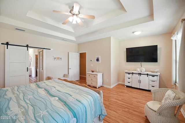 1077 Waterfall Dr, Jacksonville, FL 32225 - bedroom featuring a tray ceiling, a barn door, light wood finished floors, a ceiling fan, and baseboards