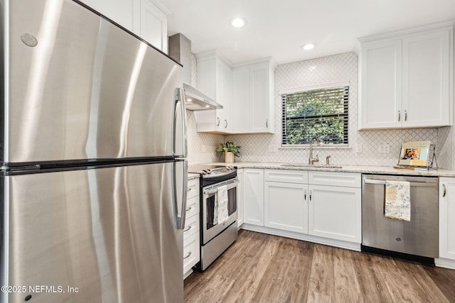 4580 Carolyn Cove Ln N, Jacksonville, FL 32258 - kitchen with stainless steel appliances, wall chimney exhaust hood, a sink, light wood-style flooring, and white cabinets