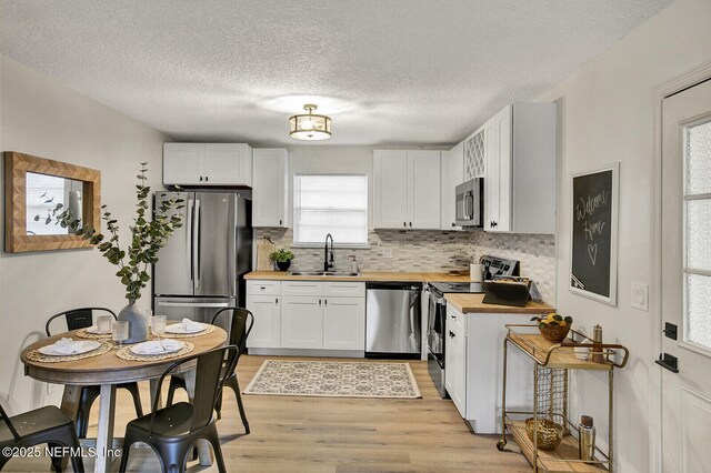 521 Talbot Ave, Jacksonville, FL 32205 - kitchen with appliances with stainless steel finishes, butcher block countertops, a sink, light wood finished floors, and decorative backsplash