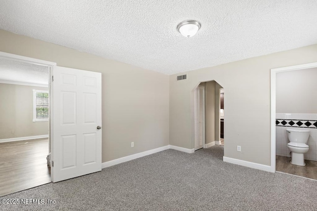 2718 Parkrus Ln, Jacksonville, FL 32208 - unfurnished bedroom featuring arched walkways, carpet flooring, a textured ceiling, ensuite bathroom, and tile walls