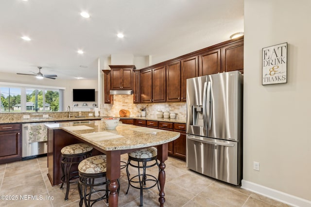32479 Willow Parke Cir, Fernandina Beach, FL 32034 - kitchen with appliances with stainless steel finishes, a center island, backsplash, light stone countertops, and under cabinet range hood