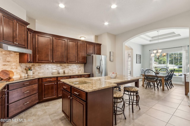 32479 Willow Parke Cir, Fernandina Beach, FL 32034 - kitchen featuring stainless steel fridge, under cabinet range hood, arched walkways, black electric cooktop, and a breakfast bar