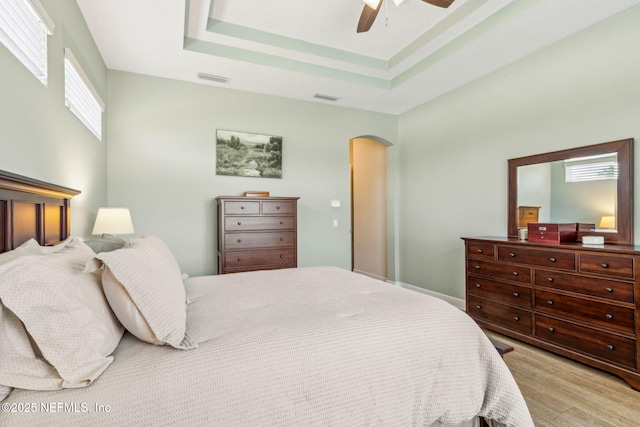 32479 Willow Parke Cir, Fernandina Beach, FL 32034 - bedroom with arched walkways, light wood-type flooring, a tray ceiling, and a ceiling fan