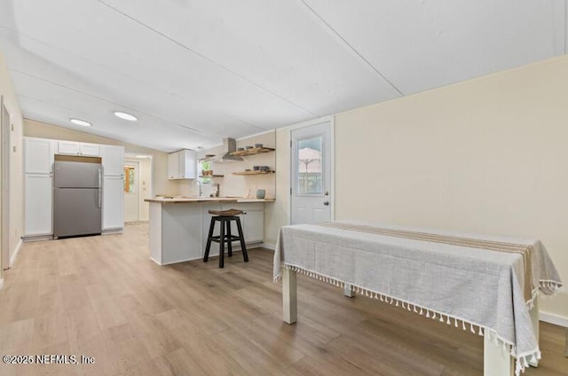 2022 Guava Ln, Bunnell, FL 32110 - kitchen with freestanding refrigerator, a breakfast bar area, white cabinetry, light wood-type flooring, and lofted ceiling