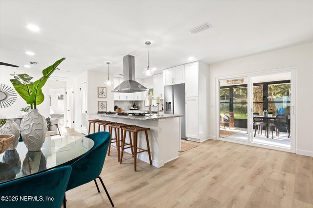 1129 Sebago Ave N, Jacksonville, FL 32233 - kitchen with island exhaust hood, stainless steel fridge with ice dispenser, a breakfast bar area, baseboards, and light wood-style flooring