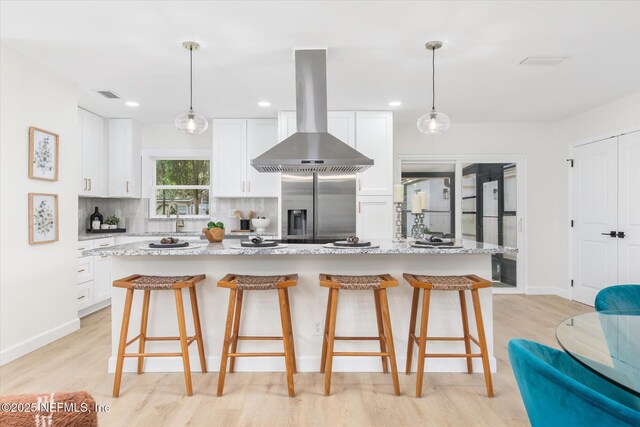 1129 Sebago Ave N, Jacksonville, FL 32233 - kitchen with range hood, stainless steel fridge, light wood finished floors, decorative backsplash, and a breakfast bar area