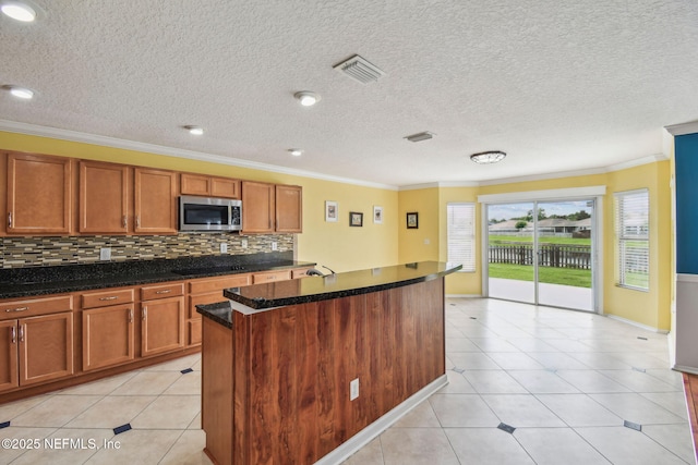 116 Nunna Rock Trl, Saint Augustine, FL 32092 - kitchen with stainless steel microwave, crown molding, a center island, brown cabinetry, and light tile patterned flooring