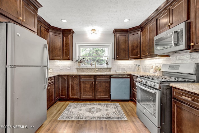 3904 Peach Dr, Jacksonville, FL 32246 - kitchen featuring appliances with stainless steel finishes, a sink, light stone countertops, light wood-type flooring, and a textured ceiling