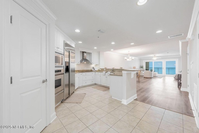 1201 1st St N Unit 1002, Jacksonville Beach, FL 32250 - kitchen featuring wall chimney exhaust hood, built in appliances, a peninsula, open floor plan, and light tile patterned flooring