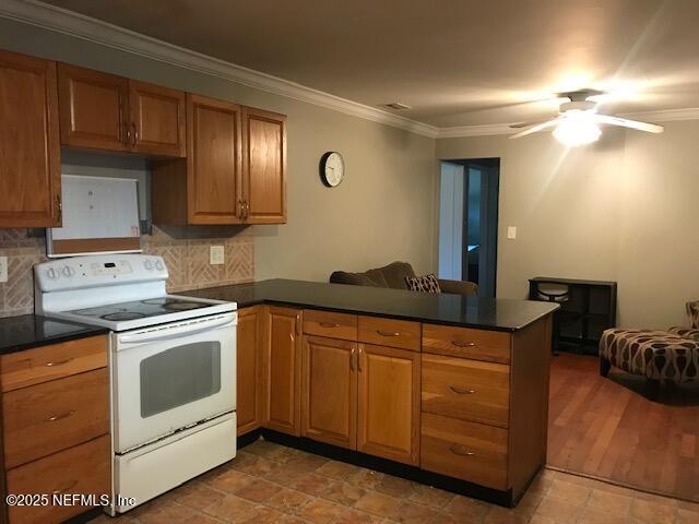 2404 Crill Ave, Palatka, FL 32177 - kitchen with white range with electric cooktop, a peninsula, dark countertops, ornamental molding, and backsplash