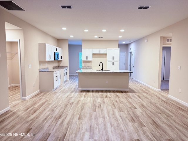 6971 Como Rd, Jacksonville, FL 32210 - kitchen with a sink, a kitchen island with sink, white cabinets, light wood-style floors, and baseboards