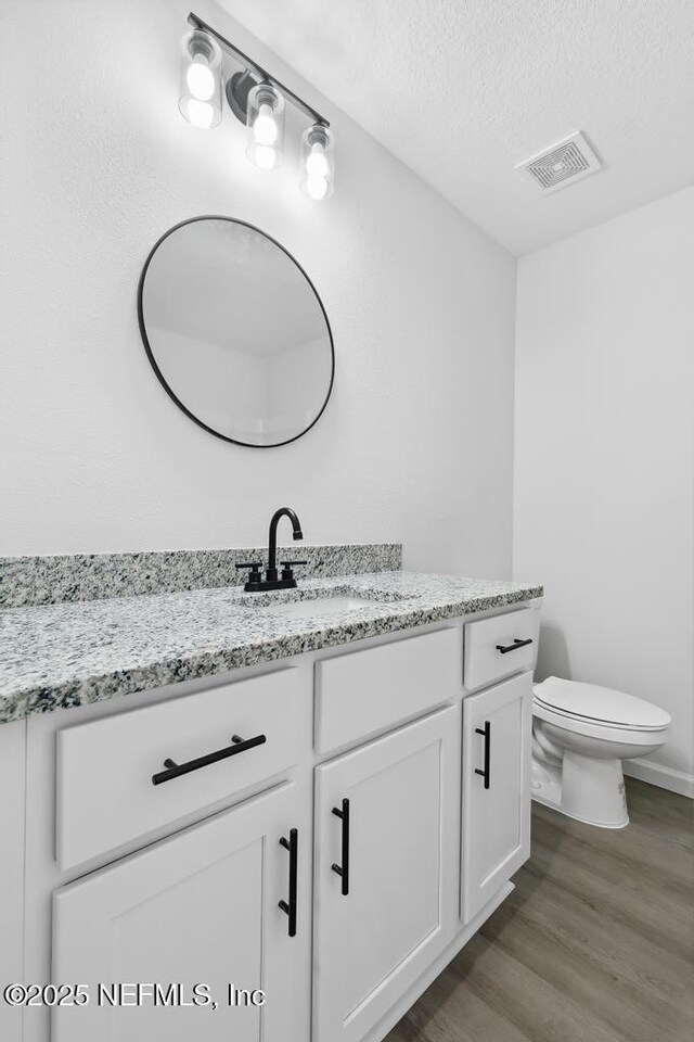 7830 Smart Ave, Jacksonville, FL 32219 - half bath featuring vanity, wood finished floors, toilet, and a textured ceiling