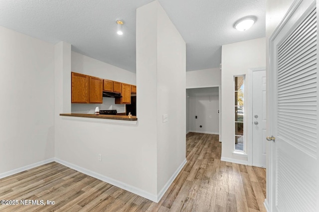 4778 Playpen Dr, Jacksonville, FL 32210 - kitchen featuring light wood-style flooring, brown cabinets, under cabinet range hood, baseboards, and a textured ceiling