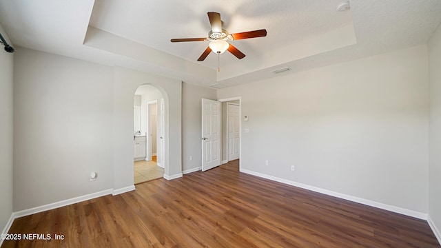 18 Amistad Dr, Saint Augustine, FL 32086 - unfurnished bedroom featuring a raised ceiling, wood finished floors, arched walkways, baseboards, and ensuite bath