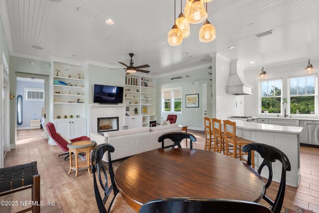 211 Tenth St, Saint Augustine, FL 32084 - dining room featuring crown molding, light wood-type flooring, a fireplace, a ceiling fan, and built in features
