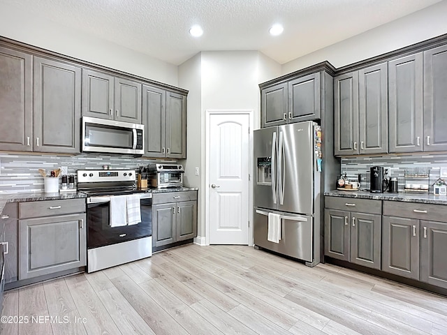 9413 Alma St, Jacksonville, FL 32220 - kitchen featuring appliances with stainless steel finishes, decorative backsplash, light wood finished floors, dark stone countertops, and a textured ceiling
