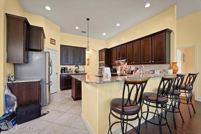 9955 Kings Crossing Dr E, Jacksonville, FL 32219 - kitchen featuring a peninsula, light stone counters, stainless steel appliances, dark brown cabinets, and recessed lighting
