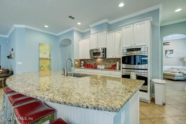 167 Royal Lake Dr, Ponte Vedra, FL 32081 - kitchen with a sink, appliances with stainless steel finishes, light stone counters, tasteful backsplash, and white cabinetry
