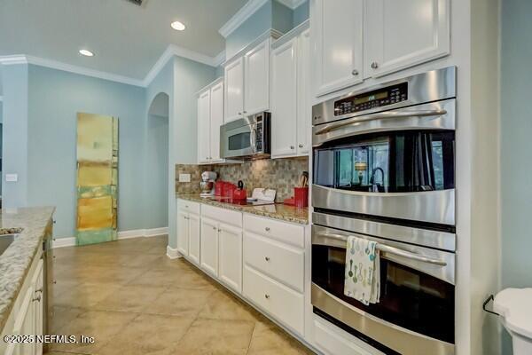 167 Royal Lake Dr, Ponte Vedra, FL 32081 - kitchen with appliances with stainless steel finishes, crown molding, arched walkways, white cabinets, and backsplash