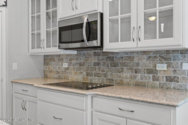 356 Heron Landing Rd, Saint Johns, FL 32259 - kitchen with stainless steel microwave, black electric cooktop, white cabinetry, glass insert cabinets, and backsplash