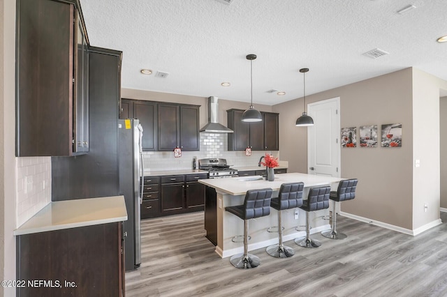 54 Pepperpike Way, Saint Augustine, FL 32092 - kitchen featuring wall chimney exhaust hood, stainless steel gas stove, a kitchen breakfast bar, light wood finished floors, and a textured ceiling
