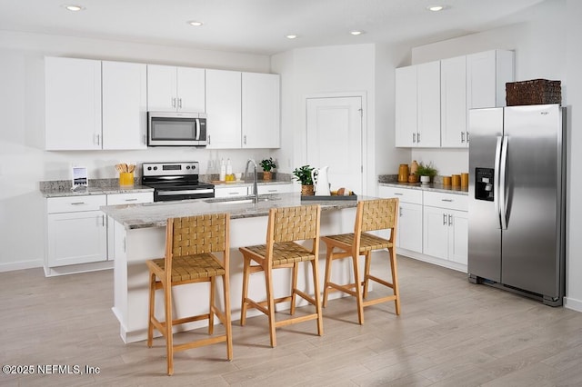 19 Sandy Ln, Palm Coast, FL 32164 - kitchen with stainless steel appliances, light wood finished floors, a kitchen island with sink, a kitchen bar, and white cabinetry