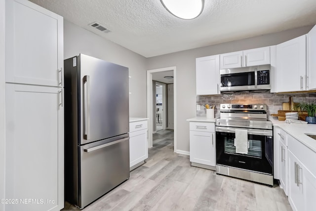 5916 Redberry Ln, Jacksonville, FL 32211 - kitchen with appliances with stainless steel finishes, light countertops, a textured ceiling, white cabinets, and light wood-style flooring
