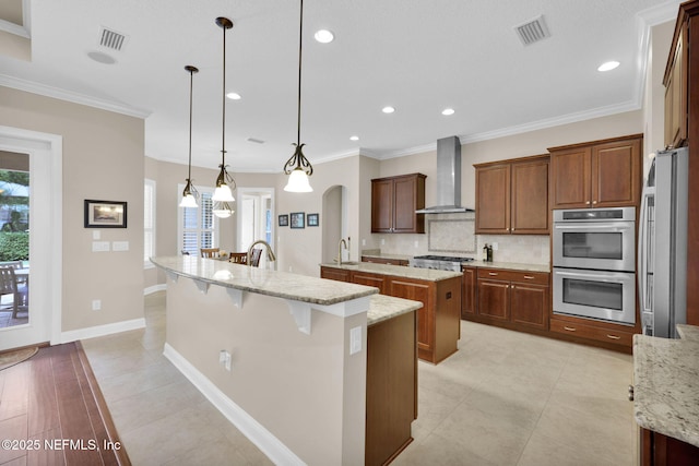 104 Hickory Hill Dr, Saint Augustine, FL 32095 - kitchen featuring wall chimney range hood, stainless steel appliances, a large island with sink, tasteful backsplash, and decorative light fixtures
