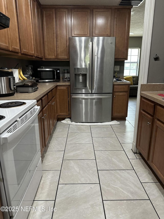 3856 Spring Park Rd, Jacksonville, FL 32207 - kitchen featuring stainless steel appliances, ventilation hood, light tile patterned floors, a textured ceiling, and brown cabinetry