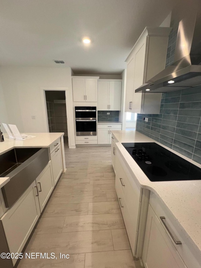 96088 Pirates Bluff Rd, Yulee, FL 32097 - kitchen with wall chimney exhaust hood, black electric cooktop, decorative backsplash, stainless steel double oven, and white cabinets