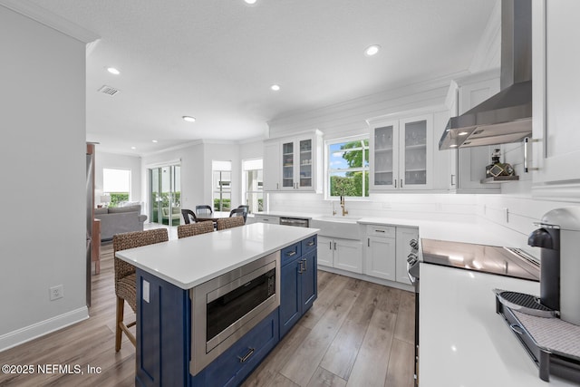 6547 Burnham Cir, Ponte Vedra Beach, FL 32082 - kitchen with blue cabinets, a sink, a kitchen bar, wall chimney range hood, and stainless steel microwave