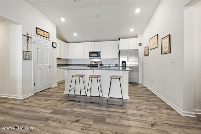 403 Boulder Ln, Jacksonville, FL 32259 - kitchen featuring appliances with stainless steel finishes, vaulted ceiling, white cabinets, an island with sink, and wood finished floors