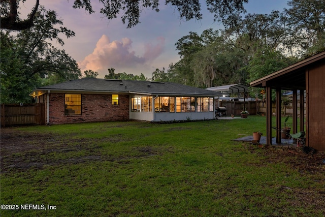 884 Live Oak Ln, Fleming Island, FL 32003 - back of house at dusk featuring a fenced backyard, a carport, a sunroom, and brick siding