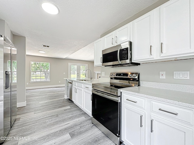 12406 Eagles Claw Ln, Jacksonville, FL 32225 - kitchen featuring stainless steel appliances, a sink, a textured ceiling, white cabinetry, and light wood finished floors