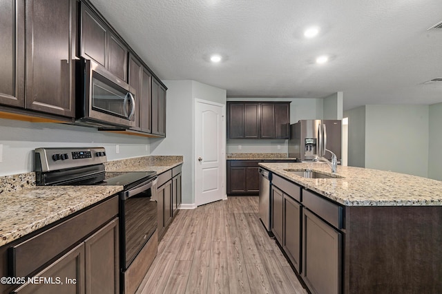 8552 Lake George Cir W, Macclenny, FL 32063 - kitchen with appliances with stainless steel finishes, a sink, light wood-style flooring, dark brown cabinetry, and a center island with sink