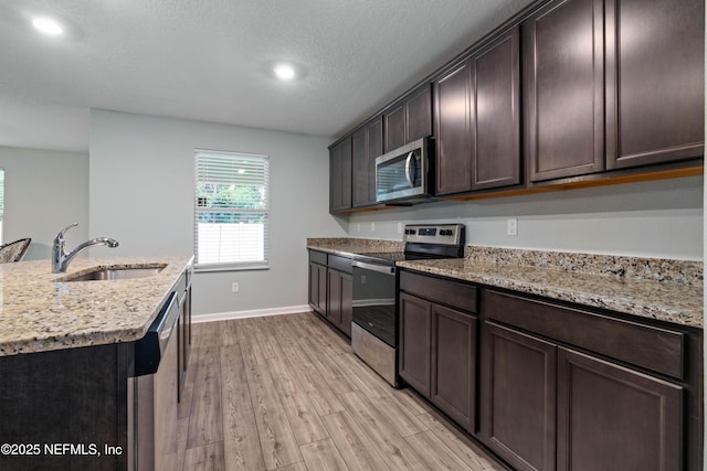 8552 Lake George Cir W, Macclenny, FL 32063 - kitchen with stainless steel appliances, a sink, light wood-type flooring, dark brown cabinetry, and light stone countertops
