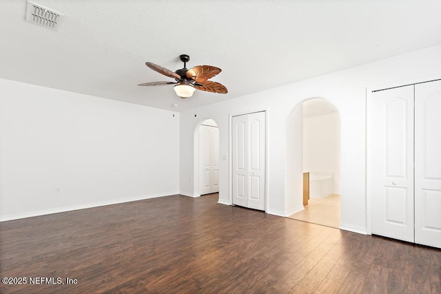 65074 Mossy Creek Ln, Yulee, FL 32097 - unfurnished bedroom with multiple closets, arched walkways, dark wood-style floors, baseboards, and ceiling fan