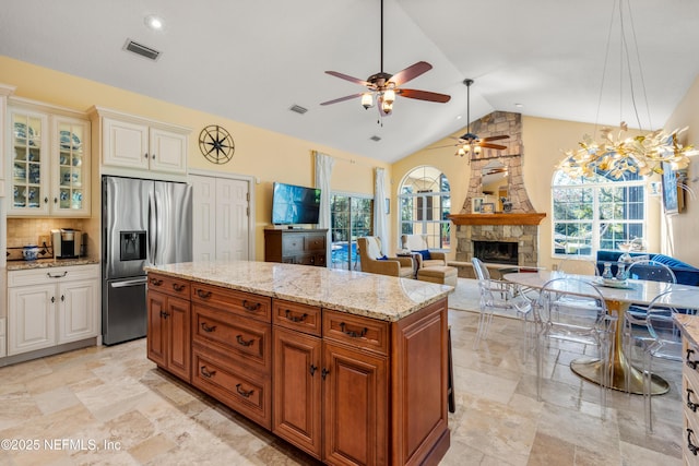 8 Rue Renoir, Palm Coast, FL 32137 - kitchen with stainless steel fridge, a fireplace, ceiling fan, light stone counters, and glass insert cabinets
