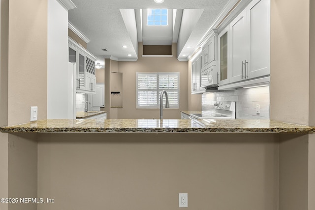 1141 Glengad, Ormond Beach, FL 32174 - kitchen with range with electric stovetop, white microwave, glass insert cabinets, decorative backsplash, and stone counters